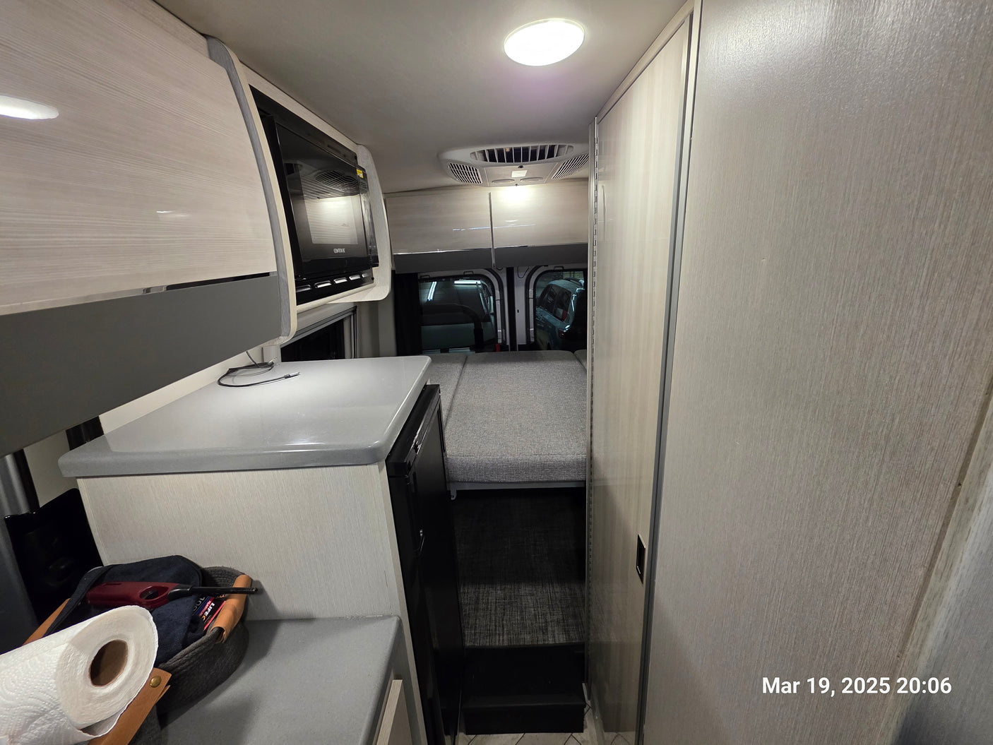 RV rental interior: light wood kitchenette, microwave, and a cozy bed area extending to the rear of the van.