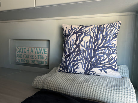 Cozy RV rental interior with blue coral pillow, soft waffle blanket, & "Catch a Wave" sign.