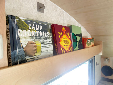 RV rental shelf holds "Camp Cocktails" & "Pendleton Field Guide to Campfire Stories" books for camp entertainment.