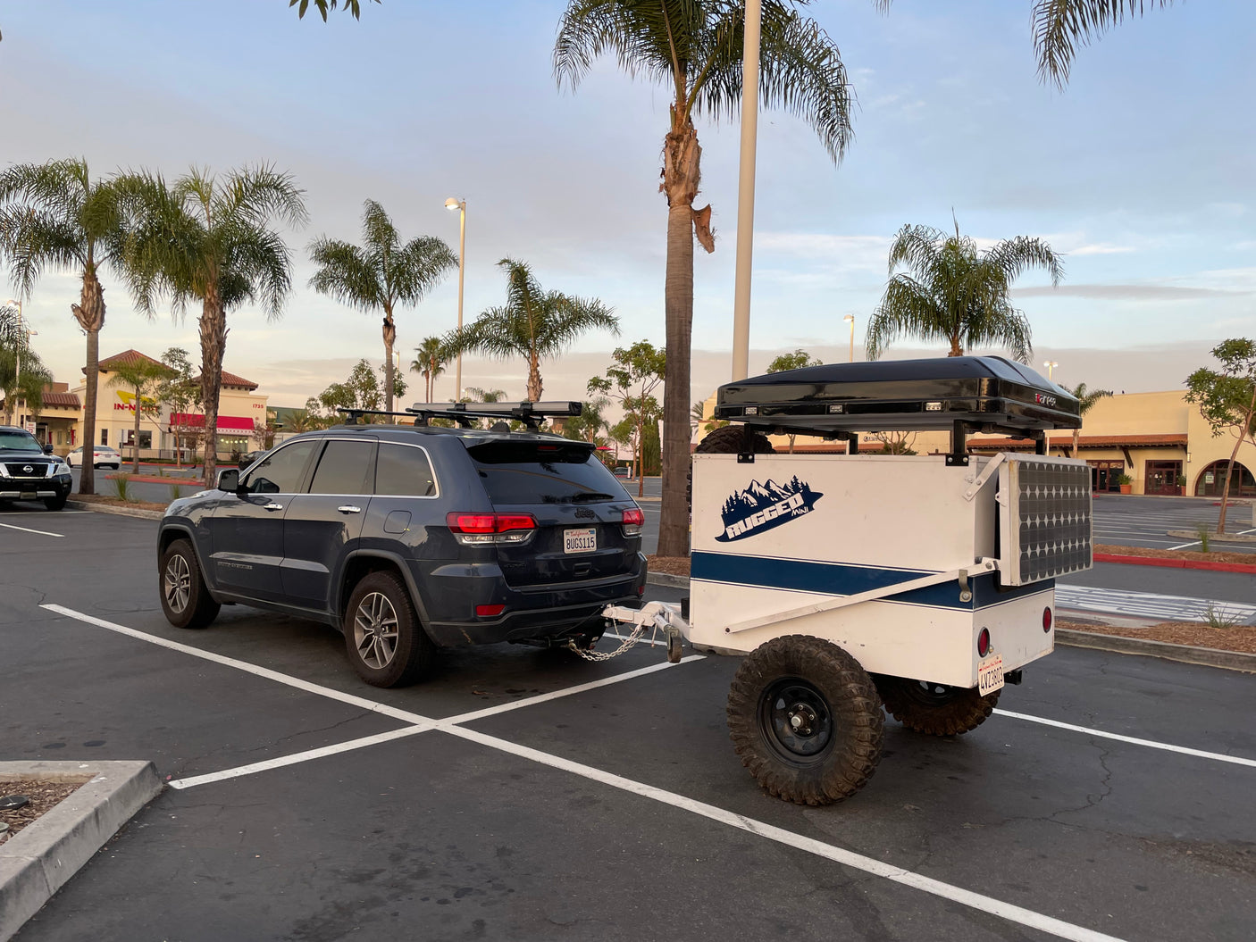 A dark blue Jeep tows an RV rental off-road trailer with a rooftop tent, prepped for camping adventure.