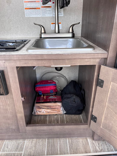 RV rental kitchen: sink, stove, and organized storage with fire starter, first aid kit, & camping supplies.
