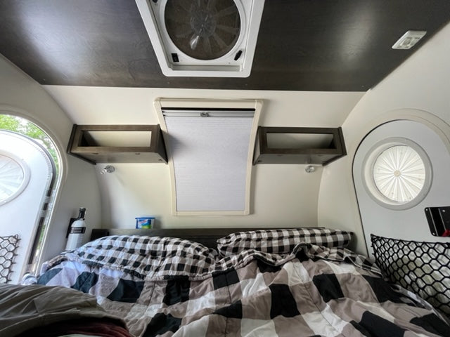 Inside a comfy RV rental: bed with plaid bedding, overhead shelves, & windows for natural light.