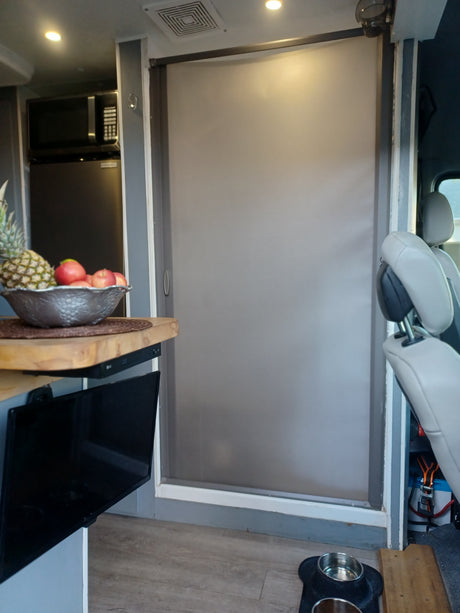 Interior of an RV rental featuring a large deployed window blind, pet bowls, fruit bowl, TV, and a microwave oven.