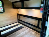 RV rental interior featuring a wood-paneled bedroom, raised bed platform with storage, and overhead cabinets.