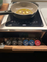RV rental kitchen: Pan with garlic & oil on induction cooktop. Pull-out spice rack features Morton & Bassett herbs.