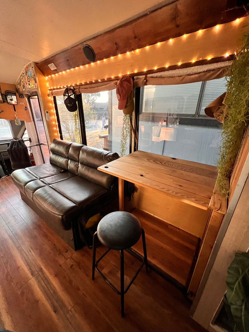 Cozy RV rental interior with a comfy leather couch, wooden table, and warm string lights. Perfect mobile home. — photo 18
