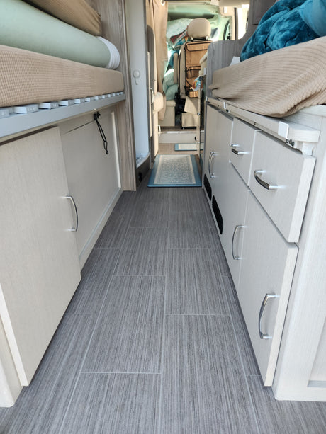 This RV rental interior features modern light wood cabinets, an organized sleeping area, and sleek gray wall panels.