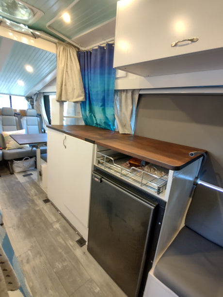 RV rental interior: Compact kitchenette with wood counter, fridge, overhead cabinets, and comfortable seating area.