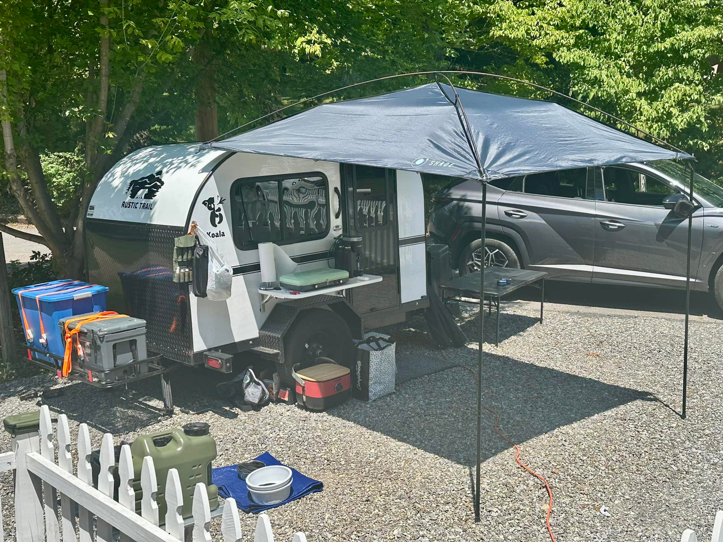 Experience comfortable camping with this RV rental: a compact teardrop camper with an awning and outdoor kitchen setup at a sunny campsite.