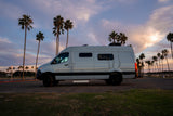 White rv rental van parked at sunset with palm trees and a vibrant sky, ready for your next journey.