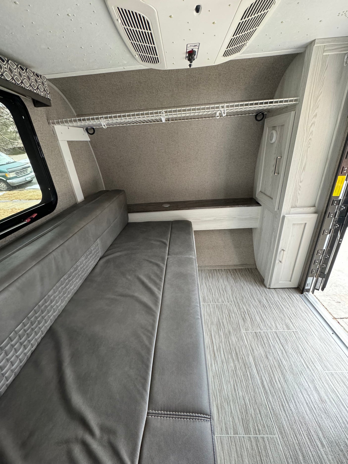 RV rental interior shows grey dinette/bed, ceiling AC, wire shelf, and light wood-look flooring.