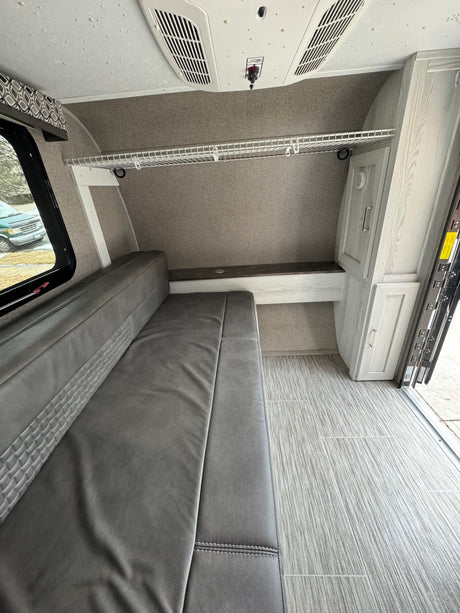 RV rental interior shows grey dinette/bed, ceiling AC, wire shelf, and light wood-look flooring.
