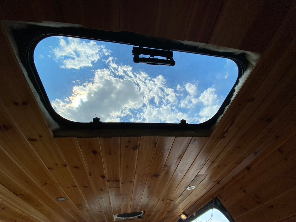 RV rental interior: A wooden ceiling features a large skylight showing a bright blue sky with white clouds.