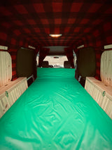 Cozy camper van interior: vibrant green bed, plaid ceiling, and wooden storage for a comfortable RV rental experience.