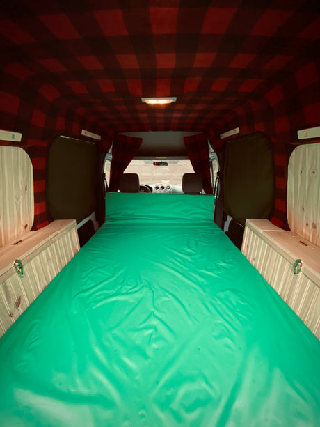 Cozy camper van interior: vibrant green bed, plaid ceiling, and wooden storage for a comfortable RV rental experience.