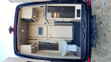 Custom RV rental interior from the rear: luxury camper van with kitchenette, toilet, storage, and wood flooring.