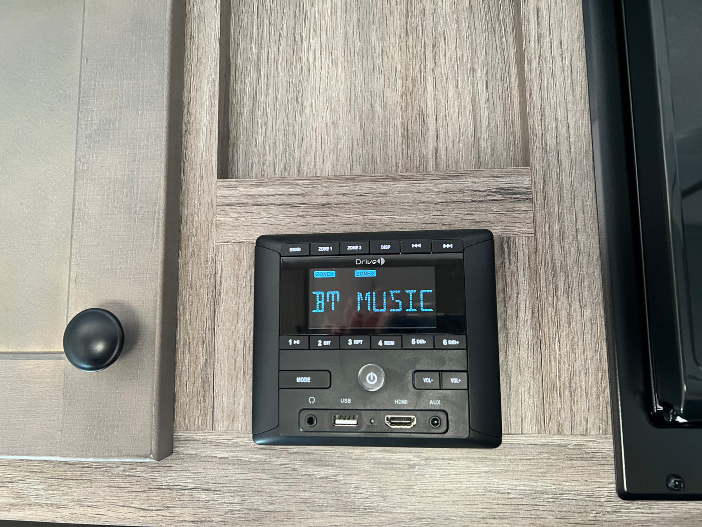An RV rental entertainment system, featuring a Drive-brand stereo displaying "BT MUSIC" on a wood-grain cabinet, with USB, HDMI, and AUX ports.