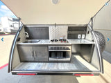 RV rental with a compact outdoor kitchen: sink, stove, microwave, storage, & counter space. Ready for adventures!