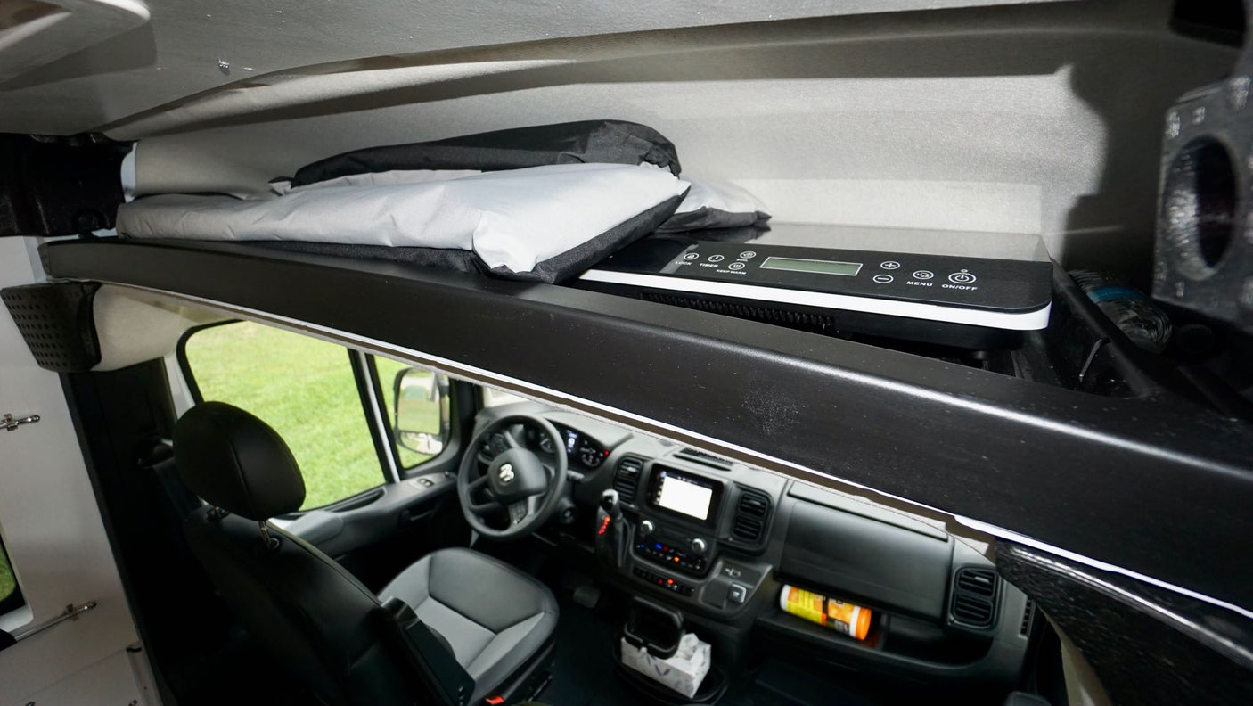 Inside an rv rental: the driver's cabin below a bunk holding folded bedding and a portable induction cooktop.