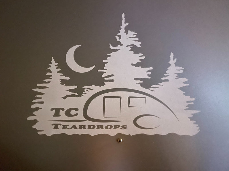 TC Teardrops RV rental graphic: A light silhouette of a teardrop trailer, pine trees, and moon on a dark wall. — photo 10