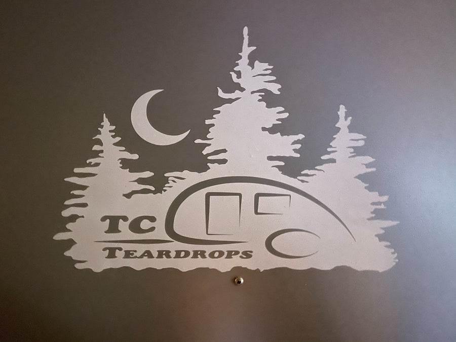 TC Teardrops RV rental graphic: A light silhouette of a teardrop trailer, pine trees, and moon on a dark wall.