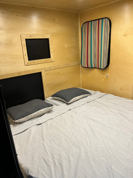 Inside an RV rental: a compact bedroom with a comfortable bed, wood-paneled walls, and privacy shades.