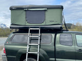 A green pickup truck with a ladder leading to a deployed Thule Tepui rooftop tent, ideal for RV rental camping.