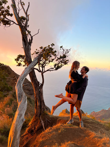 A couple embracing on a cliff at sunset, overlooking the ocean. Ideal spot after an RV rental adventure!