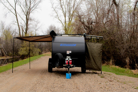 Sunray teardrop camper RV rental with an awning and privacy screen extended, parked on a gravel path by a canal.