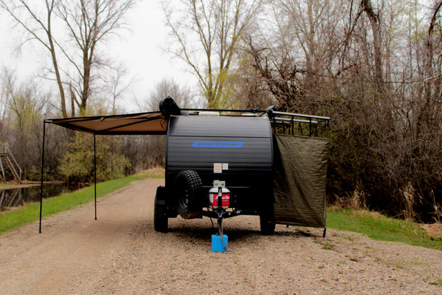 Sunray teardrop camper RV rental with an awning and privacy screen extended, parked on a gravel path by a canal.