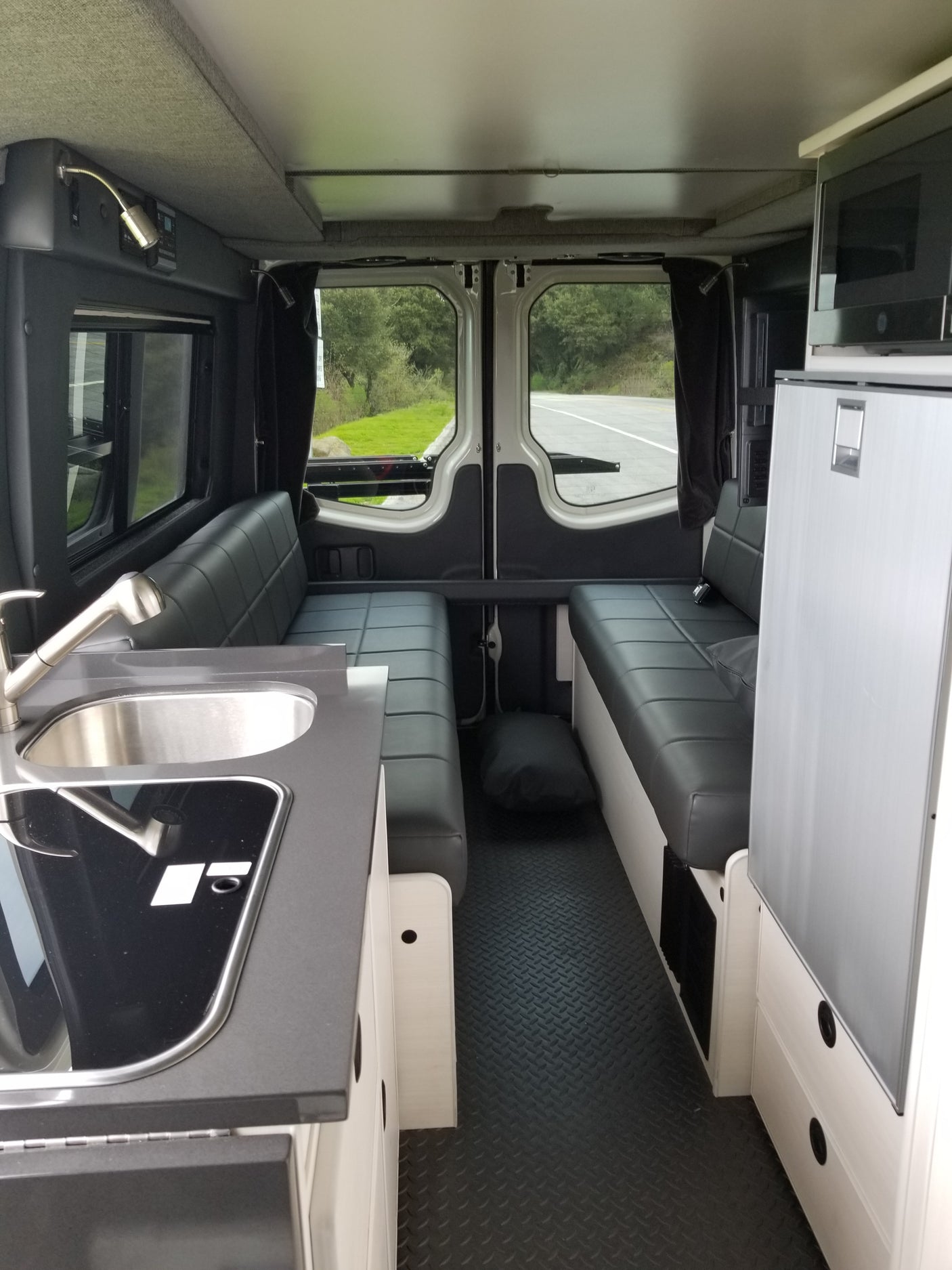 RV rental interior with modern kitchenette, dinette, fridge, microwave, and open back doors showing a road.