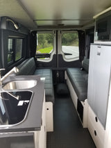 RV rental interior with modern kitchenette, dinette, fridge, microwave, and open back doors showing a road.