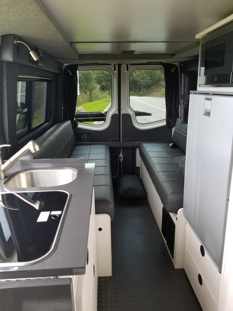 RV rental interior with modern kitchenette, dinette, fridge, microwave, and open back doors showing a road.
