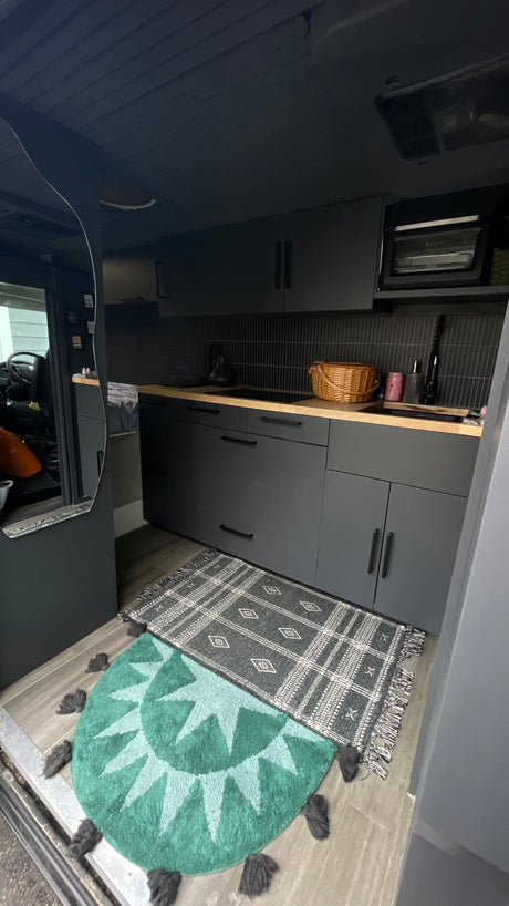 Custom RV rental kitchen with dark cabinetry, wooden counters, and stylish patterned rugs. Spacious interior for travel.