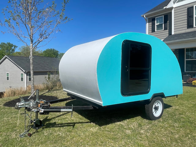 Bright blue & white teardrop camper, ideal for an RV rental, parked on a sunny green lawn.