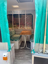 Renovated rv rental camper interior. Bright dinette with teal geometric cushions, a wood table, and clear window view.