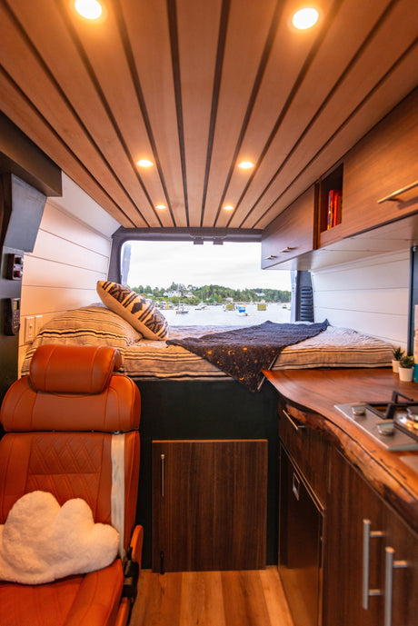 Inside this custom RV rental: wood-paneled ceiling, comfy bed, and a kitchen area, all with an ocean view.