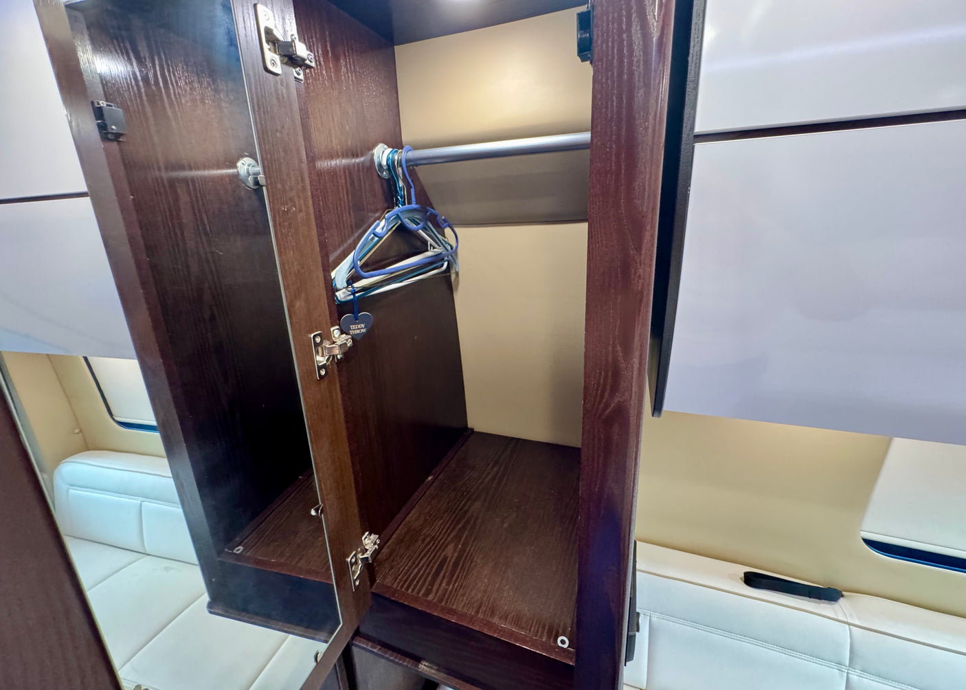 This RV rental features an open wooden closet with a hanging rod, blue hangers, and a shelf. A "Teddy Throw" tag is visible.