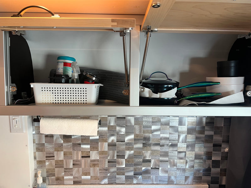 Compact kitchen storage in an rv rental with open overhead cabinets revealing organized cleaning supplies and cooking essentials. — photo 11