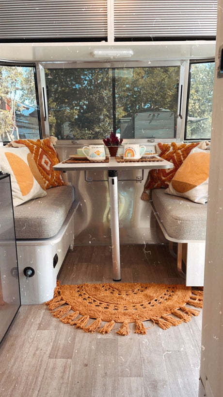 Cozy rv rental interior: inviting dinette with warm orange decor, patterned pillows, and a textured rug.