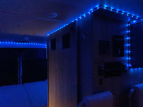 Blue LED strip lights illuminate this RV rental interior, showing the bed area and control panel details.