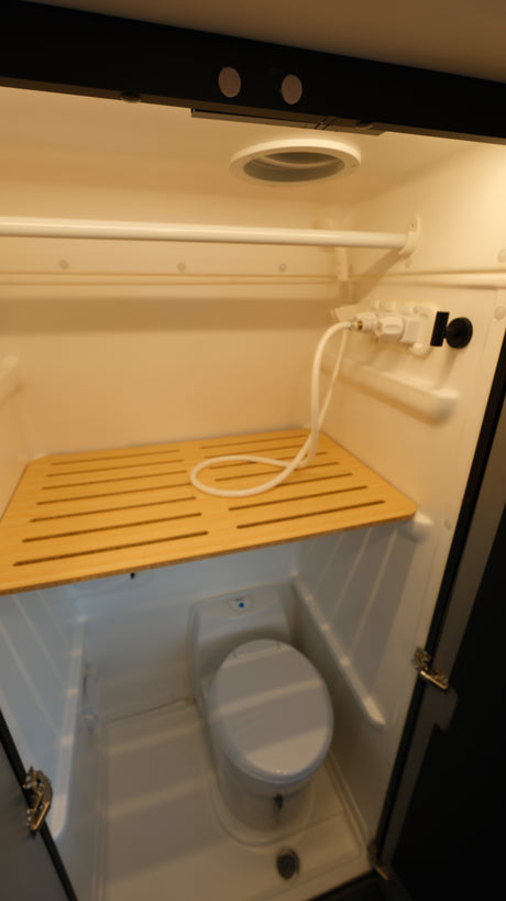 Compact RV rental bathroom with shower, toilet, and wooden mat, ideal for road trips.