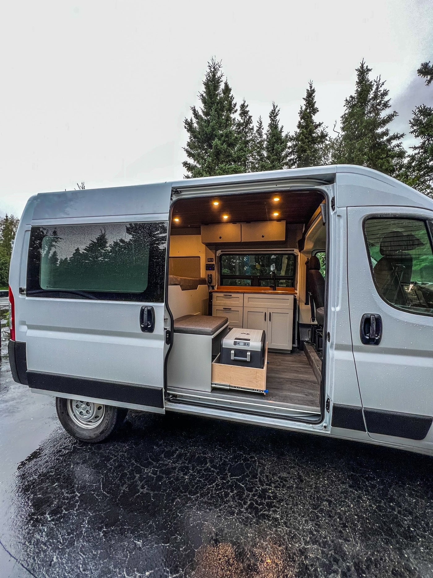 Step inside this custom RV rental, a modern camper van conversion with a cozy interior kitchen & seating area on a wet day. — photo 3