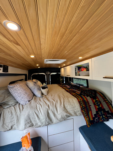 Step inside this inviting RV rental: a cozy bed, warm wooden ceiling with lights, and practical storage solutions.
