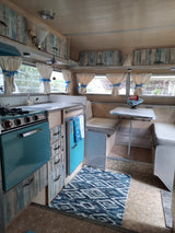 Cozy RV rental interior: dinette, teal kitchen, wood paneling, and patterned rug.