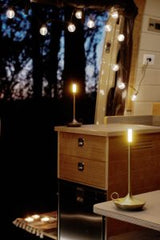 RV rental interior at night: warm string lights and modern lamps illuminate wood cabinets, offering a cozy retreat view.