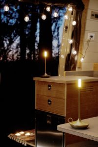 RV rental interior at night: warm string lights and modern lamps illuminate wood cabinets, offering a cozy retreat view.