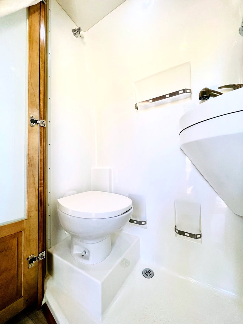 Inside an RV rental: a bright white compact wet bath with toilet, sink, & shower. Efficient space for travelers. — photo 20