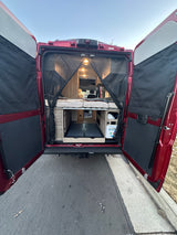 A red RV rental with its back doors open, showcasing a cozy bed, built-in storage, and mesh screen for mobile adventures.