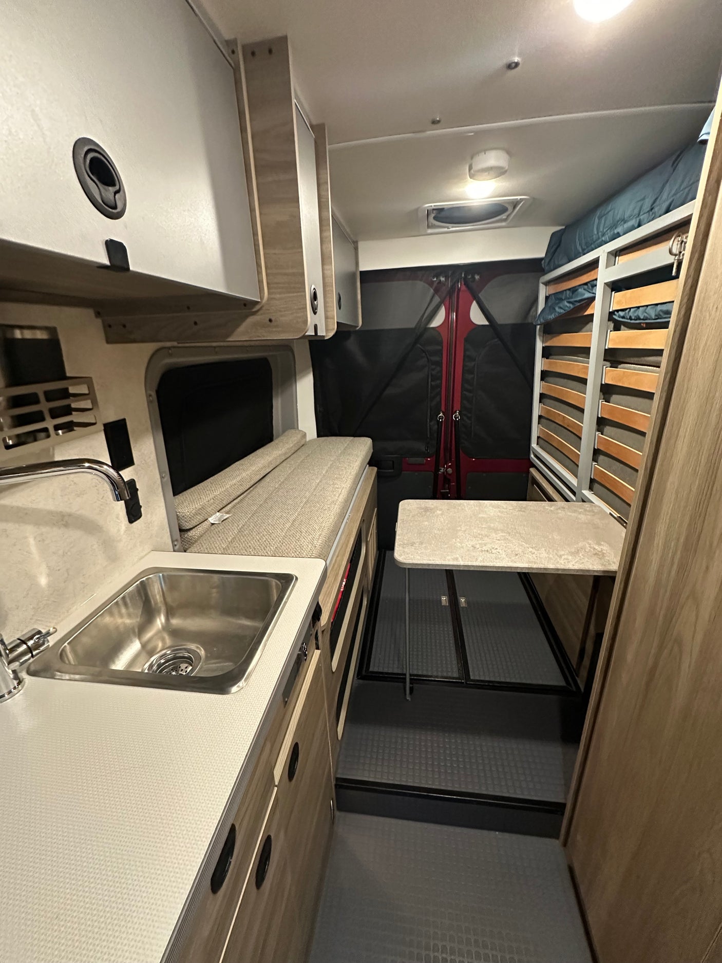 RV rental interior featuring a compact kitchen with sink, convertible bench/bed, dining table, and bunk beds.